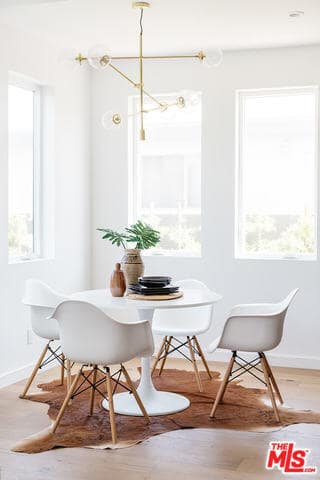 The white modern dining table has a circular shape to it that matches with the curves of the white modern dining chairs. This set stands out against the animal fur area rug over the hardwood flooring that balances the brightness of the walls and ceiling.