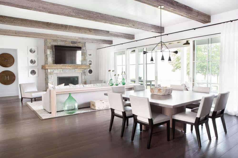 There is an ample supply of natural lighting cascading into this dining area beside the living room. This brightens up the dark hardwood flooring and the dark wooden legs of the white cushioned chairs surrounding the rectangular wooden dining table.
