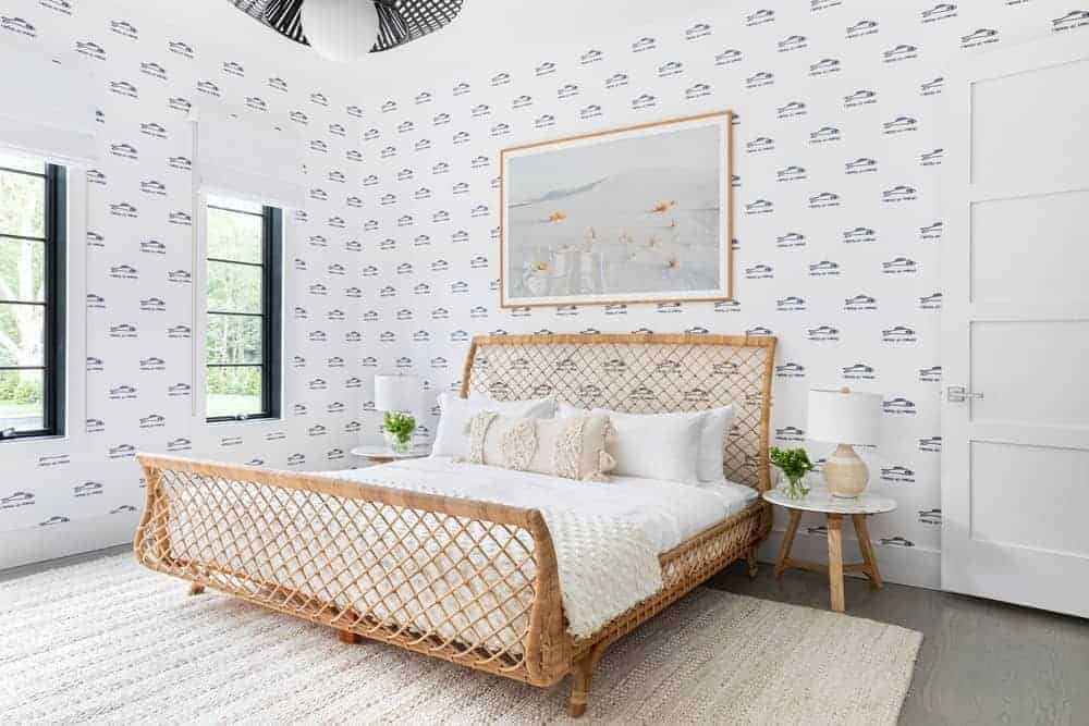 This Farmhouse-style bedroom has a large sleigh bed made of woven rattan from the foot all the way to the headboard. This works well with the white sheets of the bed and the white walls that have patterns on it.