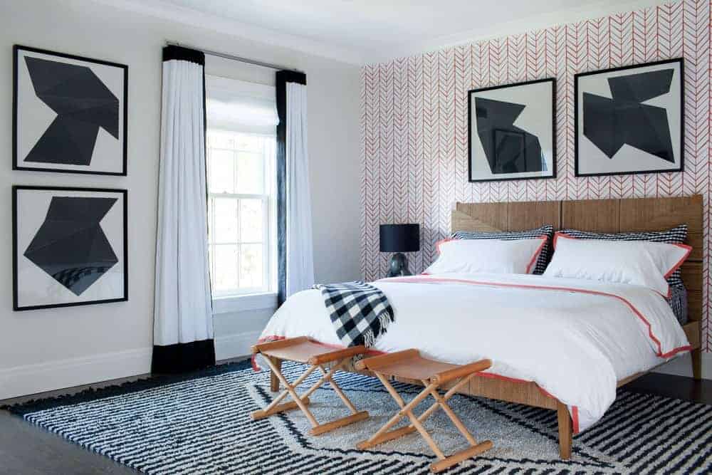 The rustic wooden traditional bed that has a wooden headboard is matched well with the two wooden foldable chairs at the foot of the bed. This is over a patterned area rug that adds a certain complexity to the room together with the red wallpaper.