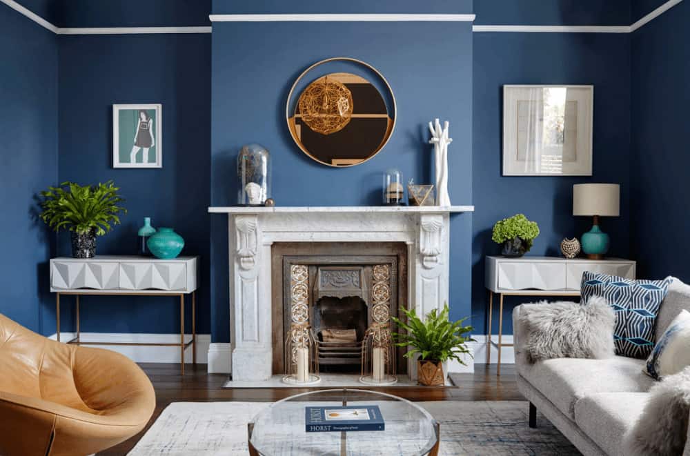 Contemporary living room decorated with white framed wall arts and a round mirror that hung above the marble fireplace flanked by white console tables.