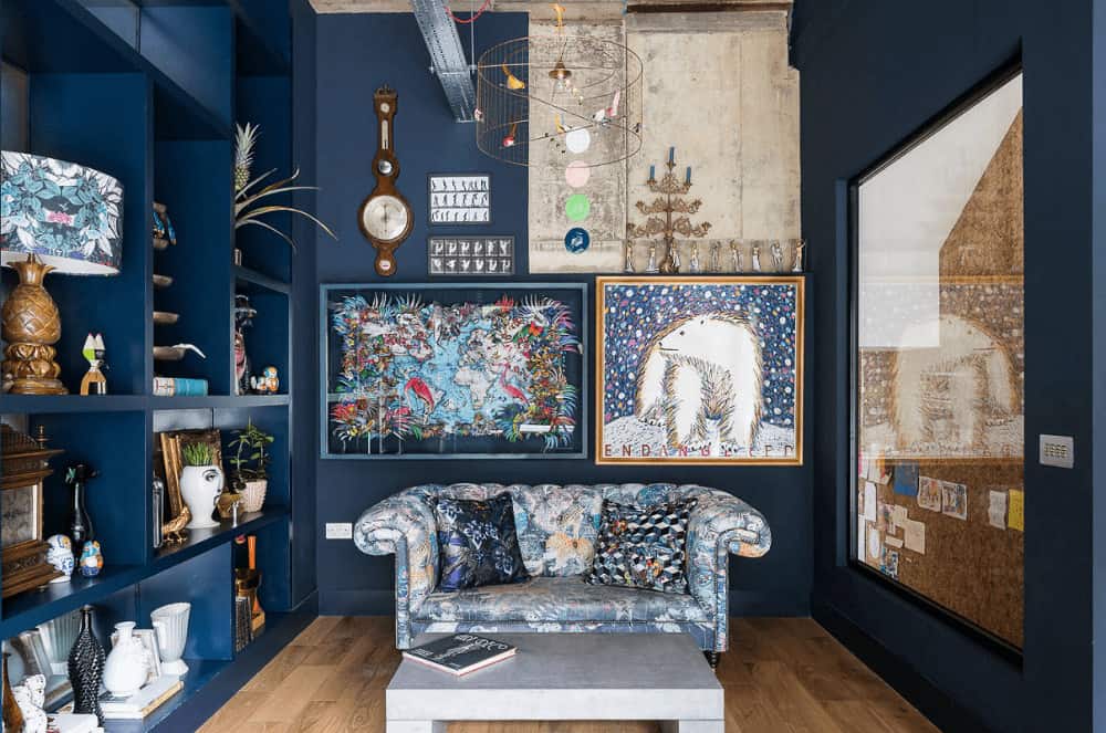 A caged chandelier illuminates this living room featuring a floral tufted sofa and a sleek coffee table over wide plank flooring. It includes gorgeous artworks and built-in shelving filled with various decors.