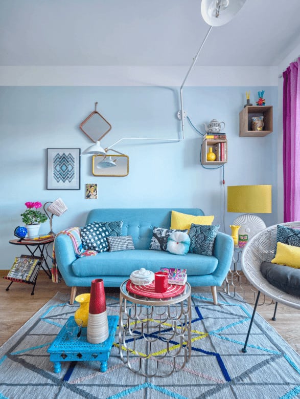 Round side tables flank a modern blue sofa paired with a stylish coffee table that sits on a textured rug. It is accompanied by floating shelves and a round chair filled with fluffy pillows.