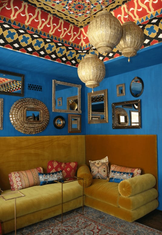 Various styled mirrors hang above the brown velvet sofa accompanied by glass top tables over a classic area rug. This room is illuminated by lantern pendants that hung from the gorgeous patterned ceiling.
