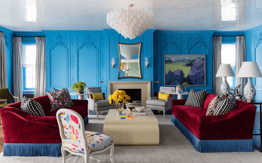 The charming living room features ornate wainscoting and high gloss ceiling mounted with a lovely semi-flush light. It includes a fireplace and mismatched seats surrounding a sleek coffee table over a gray area rug.