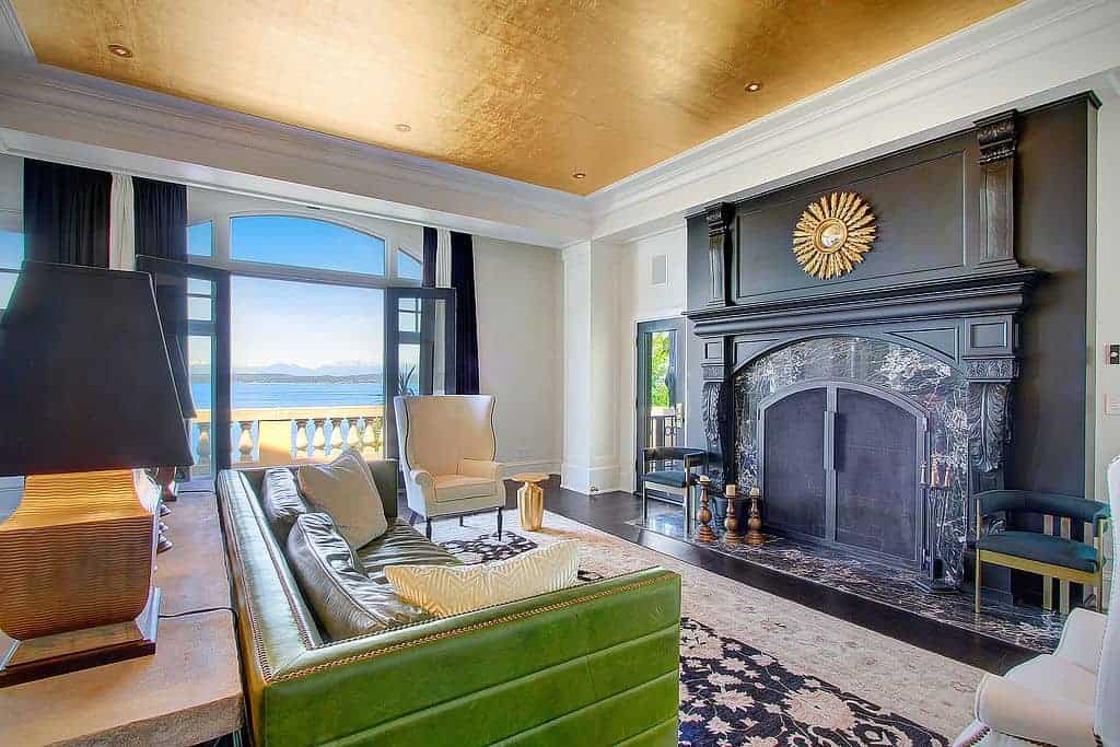 Fabulous living room with a green sofa and black fireplace decorated with a sunburst mirror. It has a gold ceiling and French door leading out to the balcony with a spectacular beach view.