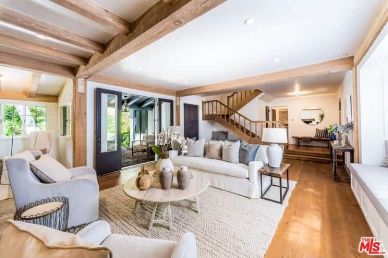Cozy living room with gray wingback chairs and a white sofa flanked by metal side tables and traditional lamps. It includes a round side table that sits on a woven area rug over the hardwood flooring.