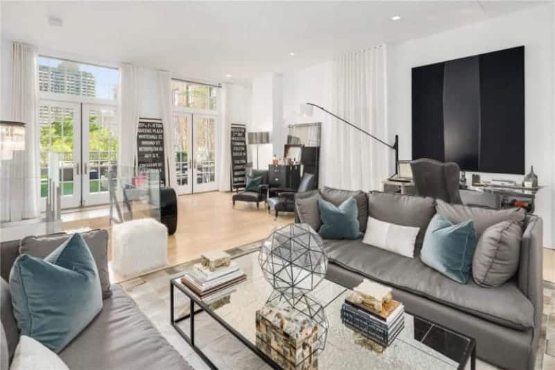 Blue velvet pillows add a nice accent to the gray sofas paired with a mirrored coffee table. This room has light hardwood flooring and French doors leading out to the green yard.