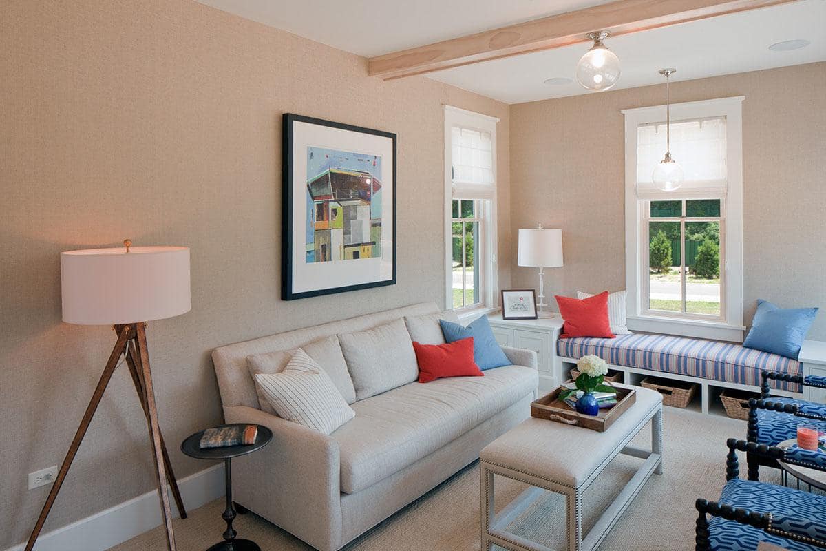 Medium-sized living room with blue patterned armchairs and a gray sofa paired with a cushioned coffee table. It includes lovely wall art and a window seat nook completed with a striped cushion and multi-colored pillows.