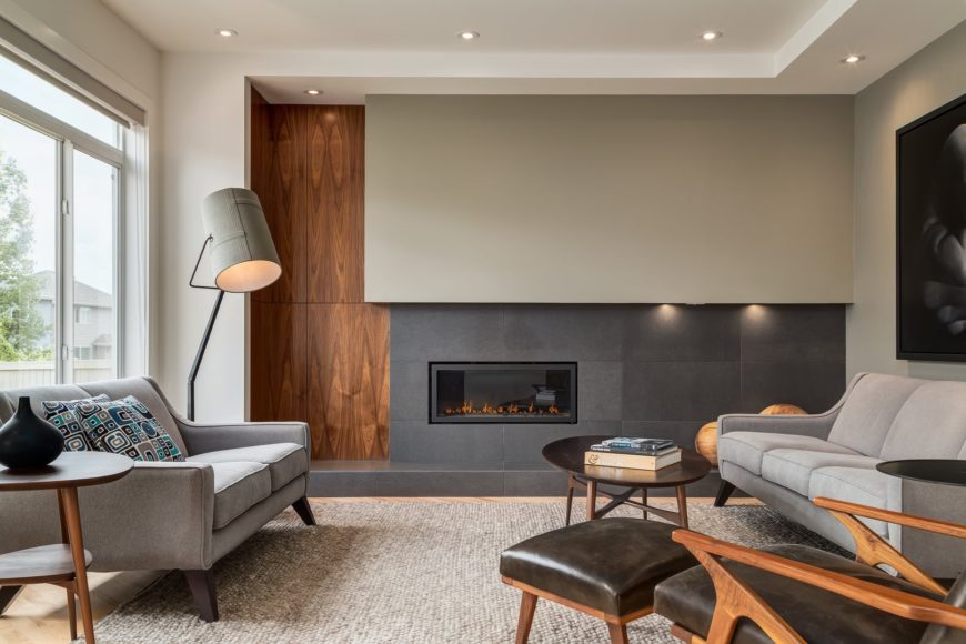 A leather lounge chair complements the round coffee table that sits on a woven area rug. This room has gray sofas and a rectangular fireplace fitted on the concrete paneled wall.